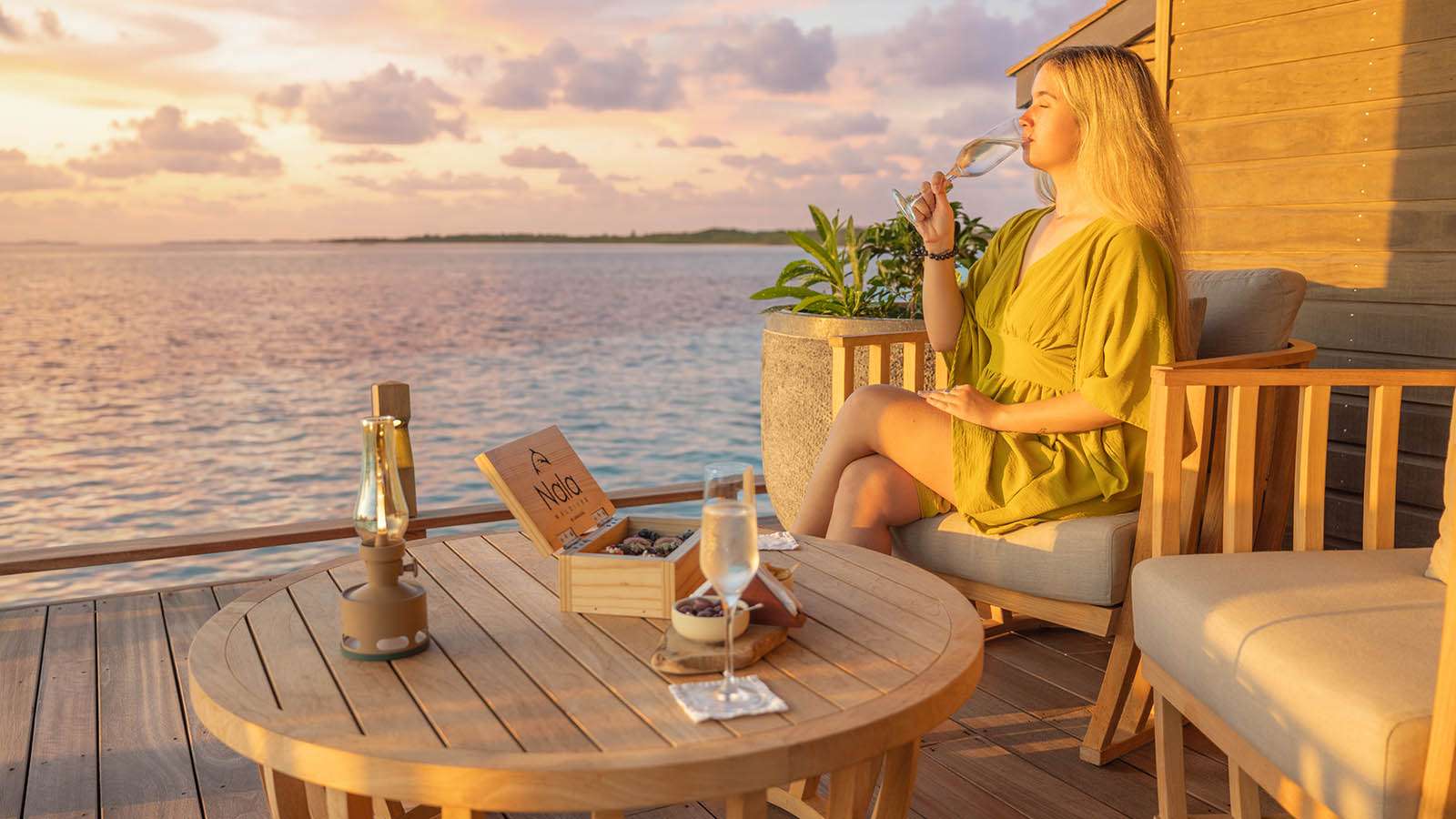 A woman drinking champagne at sunset in Bubbles bar at Nala Maldives adults only resort