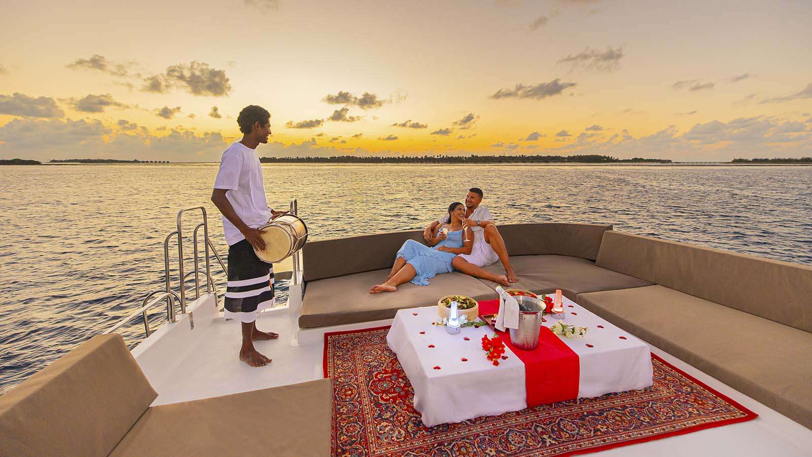 Maldives sunset with romantic couple and man playing instrument on a boat at Nala Maldives